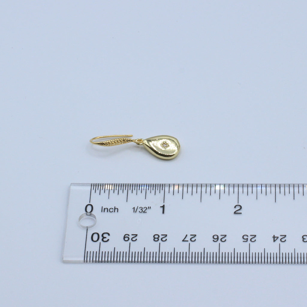 Gold teardrop-shaped pendant with a heart design on a light gray background, measured against a ruler.