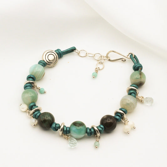 Aqua Blue Leather, hand-knotted, forms the foundation, intertwined with Agate, Amazonite, Aquamarine, and Mother of Pearl Gemstones with hand forged hook closure.