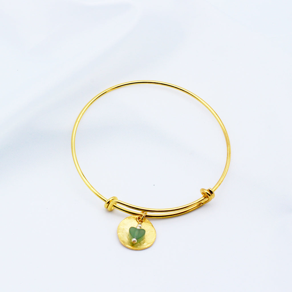 A refined hammered gold disk with a green Aventurine Gemstone dangling from an adjustable bangle.