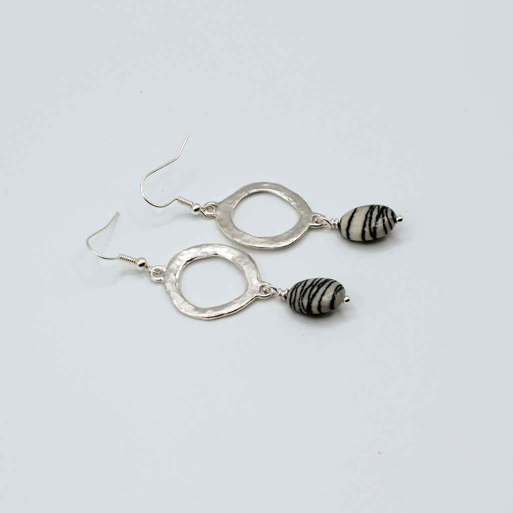 Silver earrings with black and white striped beads on a light gray background