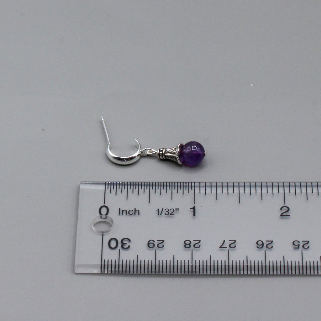 These expertly crafted earrings showcase the gentle sway of a vibrant amethyst gemstone, elegantly capped with a finely detailed pewter design. Suspended from a delicate silver hoop stud.