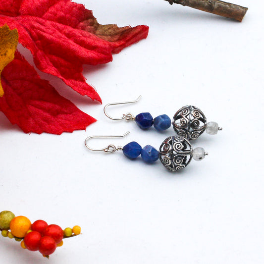 The focal point of the earrings is an intricately designed, antiqued sterling silver sphere, featuring sodalite and labradorite gemstones.