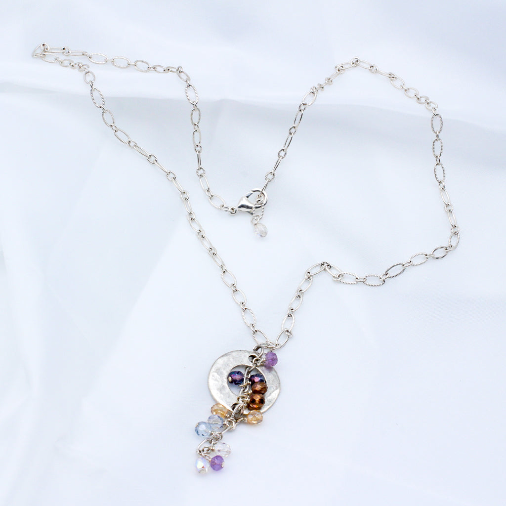 Pastel colors with a blend of delicate crystals, shimmering silver electroplated metals, and a hammered disk focal.