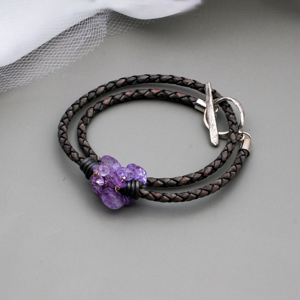 Amethyst gemstone beads twist around edgy braided dark gray leather. It is finished with a silver toggle clasp.