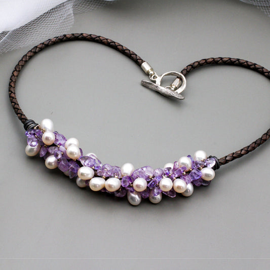 Amethyst gemstone beads and freshwater pearls twist around braided dark gray leather. It is finished with a silver toggle clasp.