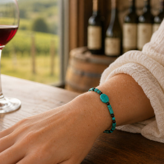 Person wearing a turquoise bracelet with wine bottles and a glass in the background