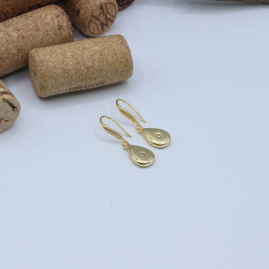 Gold earrings on a white surface with cork wine bottle stoppers in the background.