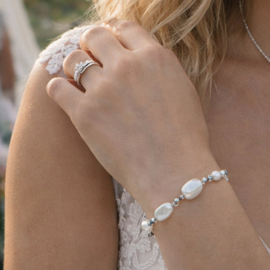 Close-up of a hand wearing a pearl bracelet and ring, with a blurred background.