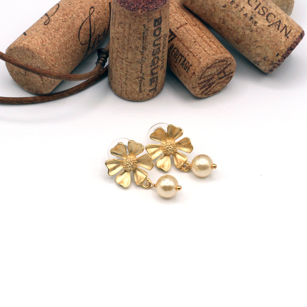 Gold floral earrings with pearl accents on a white background with wine corks.