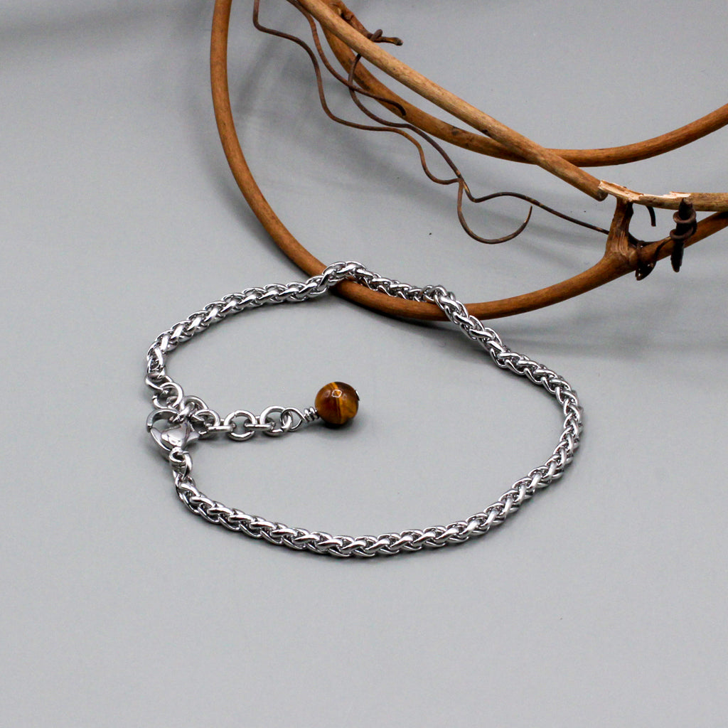 Stainless steel rope chain bracelet features a 1½-inch adjustable extension. It is secured with a lobster clasp and highlighted by a tiger eye jasper bead.