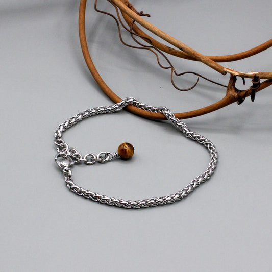 Stainless steel rope chain bracelet features a 1½-inch adjustable extension. It is secured with a lobster clasp and highlighted by a tiger eye jasper bead.